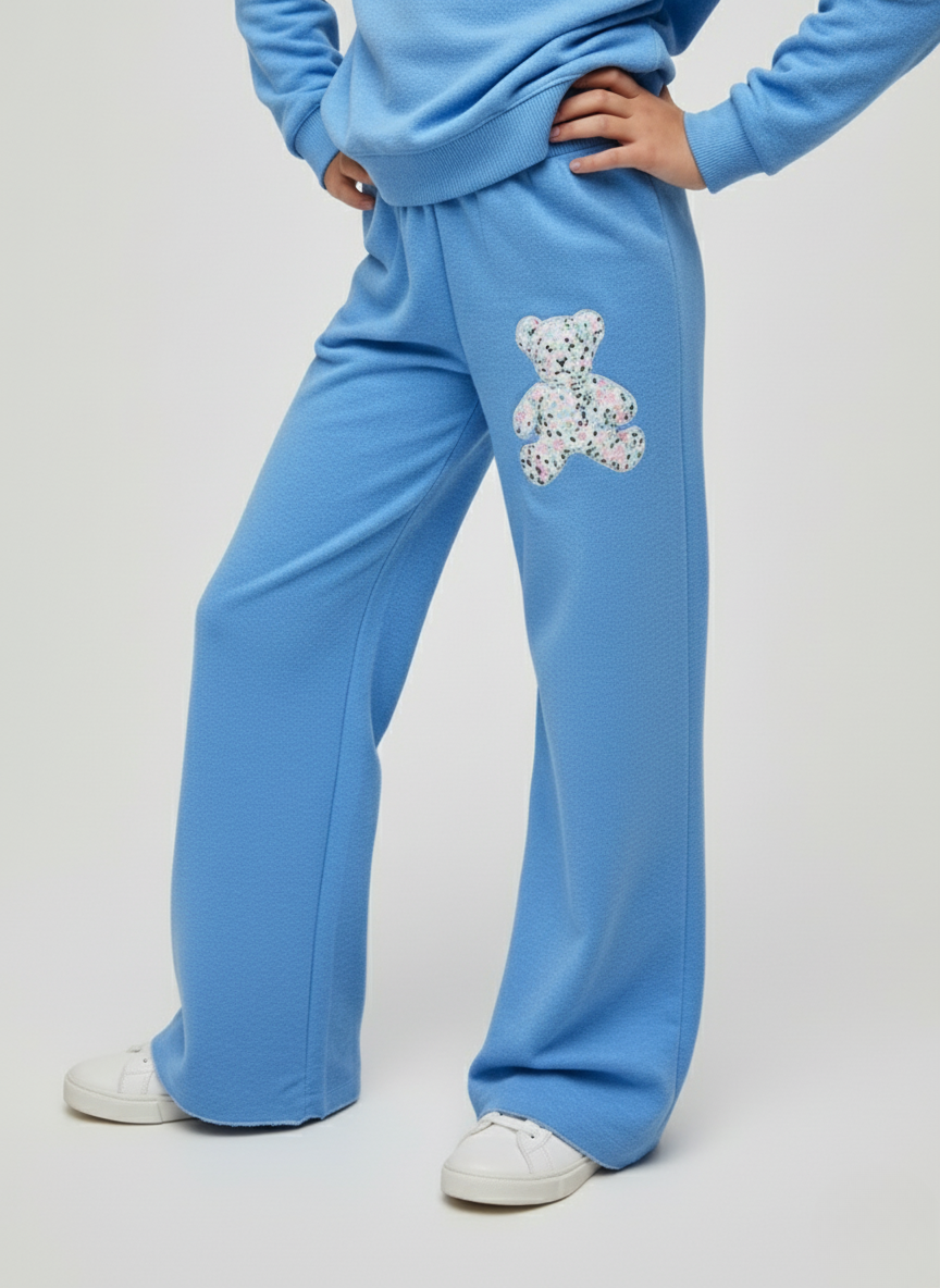 Person wearing light blue tracksuit with a decorative bear patch on a white background
